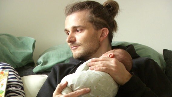 Ein junger Mann hält ein Baby auf dem Arm. © Screenshot 