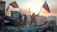 Ein Video-Standbild soll zeigen, wie Soldaten eine russische National- und eine Wagner-Flagge auf einem beschädigten Gebäude in der ukrainischen Stadt Bachmut schwenken. © dpa picture alliance / Zoonar Foto: Leonid Altman