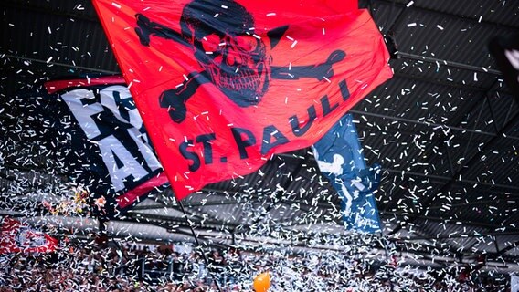 Fans des FC St. Pauli schwenken Fahnen und werfen Konfetti. © IMAGO / Noah Wedel 