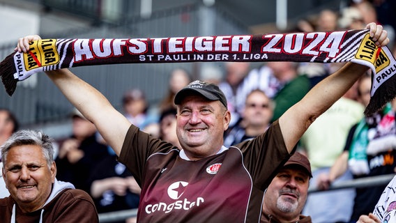 Ein Fan des FC St. Pauli hälte einen Schal mit der Aufschrift "Aufsteiger 2024" in die Höhe. © picture alliance/dpa | Axel Heimken 